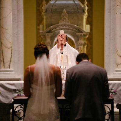 Couple kneeling before the priest elevating the Eucharist on their wedding day