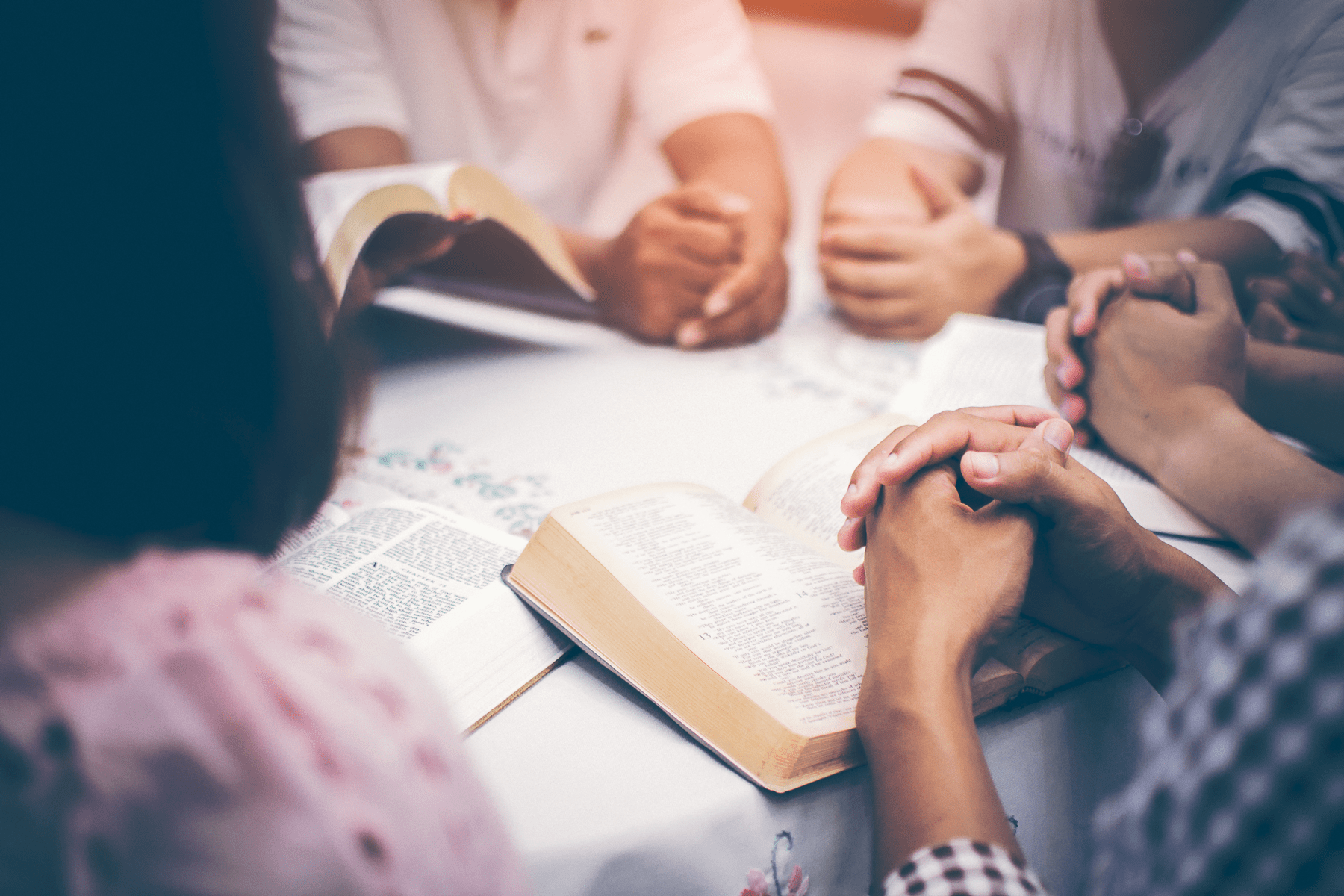 Hands folded in prayer over several Bibles