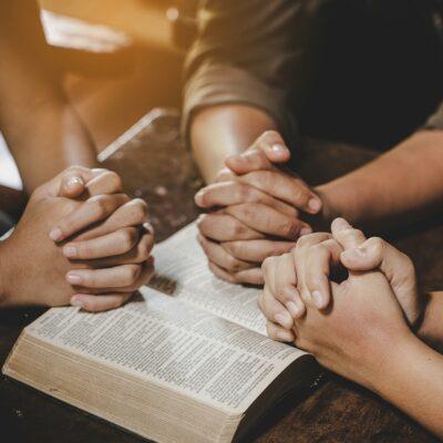 Hands folded in prayer over a Bible